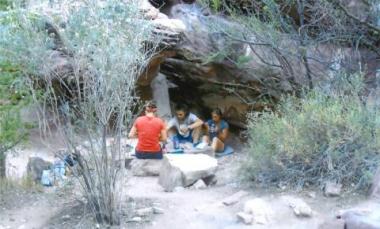 A group of students sit under a rock formation Spring