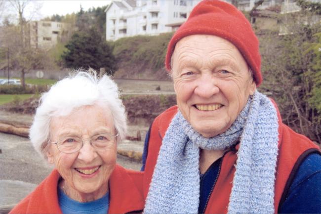 Bess and Robert Christman in matching red vests, Robert in a red beanie and purple knitted scarf