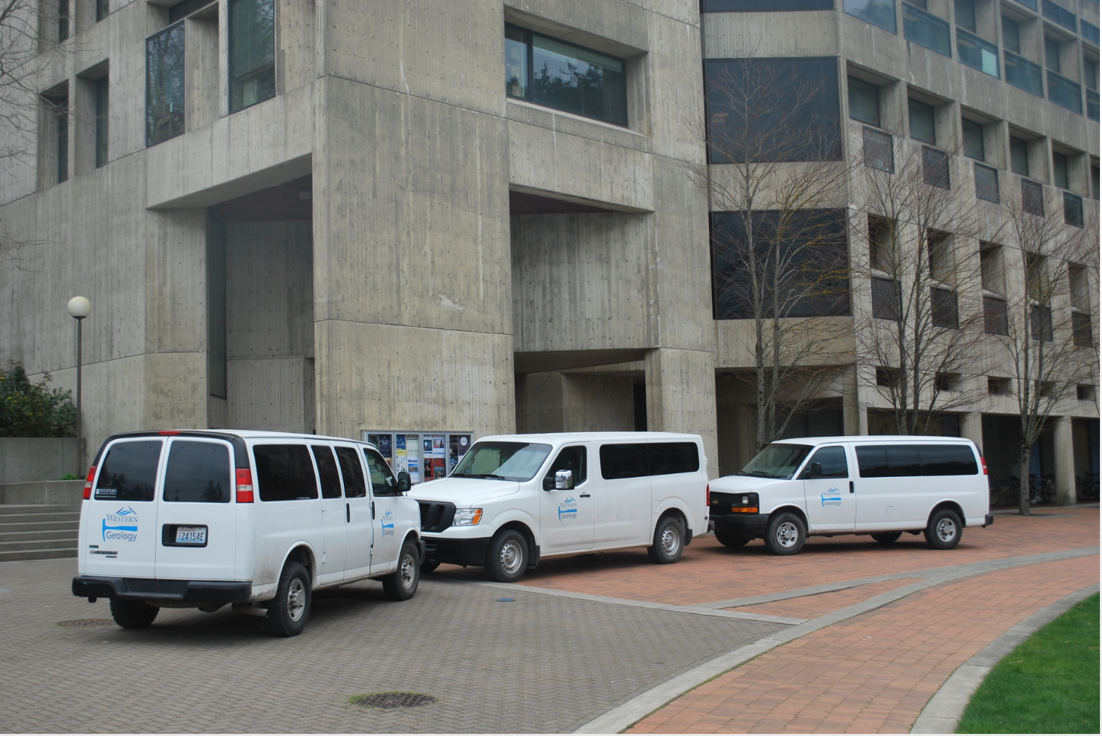 Three white Geology-branded vans parked outside the ES building